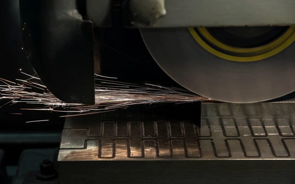 Surface grinding wheel cutting an industrial blade blank, sparks over the machine table
