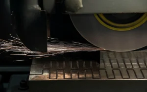 Surface grinding wheel cutting an industrial blade blank, sparks over the machine table